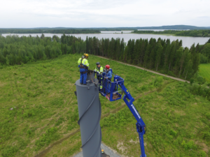 Kolme ihmistä nostettu henkilönostimella korkean piipun päälle. Yksi on siirtynyt piipun päälle turvavaljaisiin kiinnitettynä ja kaksi avustavat nostimesta käsin.